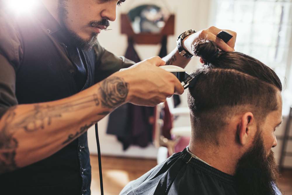barber trims the back of his client’s hair with clippers
