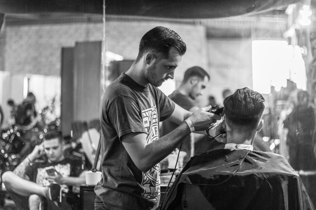 barber giving a client a haircut using clippers in a barbershop in black and white
